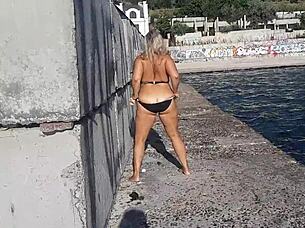 Look at that milf playing with her big tits and ass on the public beach!