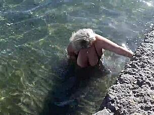 Look at that milf playing with her big tits and ass on the public beach!