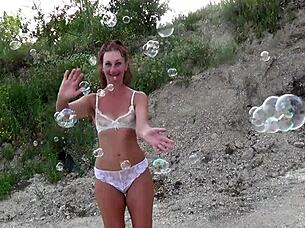 Mature amateur in see-through bikini plays with soap bubbles.